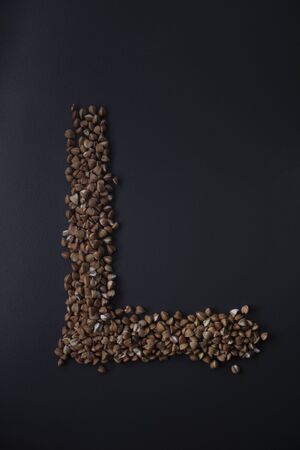 Letter 'L' written with buckwheat On gray background, top view, copy space. Food supplies crisis, food donation on quarantine isolation periodの写真素材