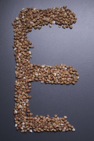 Letter E written with buckwheat On gray background, top view, copy space. Food supplies crisis, food donation on quarantine isolation periodの写真素材