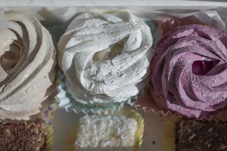Sweet homemade dessert zephyr pink, beige, white - big marshmallows and bird milk candies in a white gift box on a white table. handmade Big zephyr sprinkled with powdered sugar. Food photographyの写真素材
