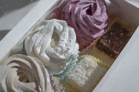 Sweet homemade dessert zephyr pink, beige, white - big marshmallows and bird milk candies in a white gift box on a white table. handmade Big zephyr sprinkled with powdered sugar. Food photographyの写真素材