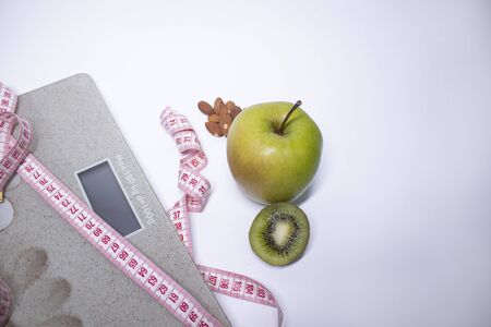 Red measuring tape, apple, kiwi and almonds near beige bathroom scales. Diet and Healthy life, loss weight, sport concept. Top view. Copy space. Isolated. White backgroundの写真素材