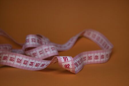 Red measuring tape on orange background. Loss weight concept. Top view. Copy space. Isolated. . High quality photoの写真素材
