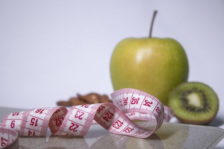 Red measuring tape, apple, kiwi and almonds on beige bathroom scales. Diet and Healthy life, loss weight, sport concept. Copy space. Isolated. White backgroundの写真素材