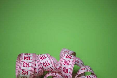 Red measuring tape on green background. Loss weight concept. Top view. Copy space. Isolated. . High quality photoの写真素材