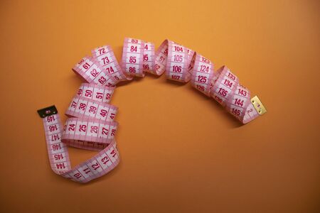 Red measuring tape on orange background. Loss weight concept. Top view. Copy space. Isolated. . High...