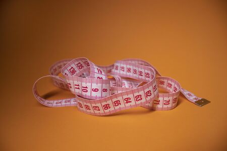 Red measuring tape on orange background. Loss weight concept. Top view. Copy space. Isolated. . High quality photoの写真素材