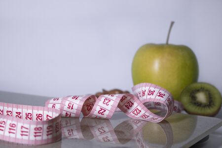 Red measuring tape, apple, kiwi and almonds on beige bathroom scales. Diet and Healthy life, loss weight, sport concept. Copy space. Isolated. White backgroundの写真素材