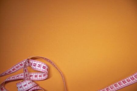 Red measuring tape on orange background. Loss weight concept. Top view. Copy space. Isolated. . High quality photoの写真素材