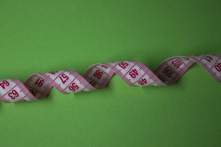 Red measuring tape on green background. Loss weight concept. Top view. Copy space. Isolated. . High quality photoの写真素材