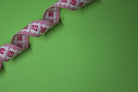 Red measuring tape on green background. Loss weight concept. Top view. Copy space. Isolated. . High quality photoの写真素材
