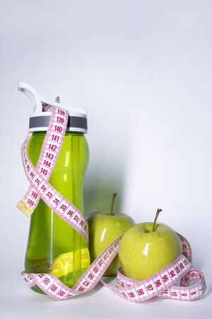 Red measuring tape over green sport bottle and green apple. Diet and Healthy life, loss weight, sport concept. Top view. Copy space. Isolated. White background. High quality photoの写真素材