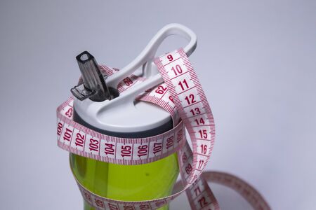 Red measuring tape over green sport bottle. Healthy life, sport concept. Top view. Copy space. Isolated. White background. High quality photoの写真素材