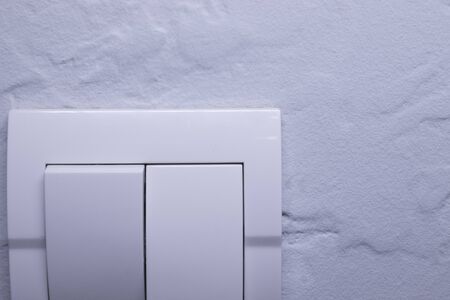 Plastic mechanical white light switch, installed on a light gray wall. High quality photo