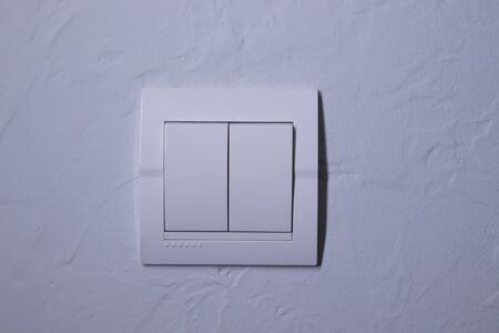 Plastic mechanical white light switch, installed on a light gray wall. High quality photo