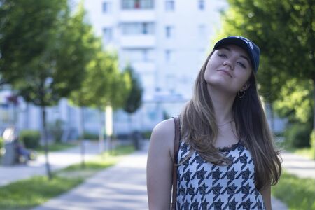 Pretty young blonde woman wearing a t-shirt, jeans shorts and cap. in a park. copy space. High...