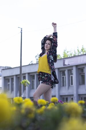 Attractive young brunette woman in yellow t-shirt and flowery shorts costume. near a bush of flowers. copy space. High quality photoの写真素材