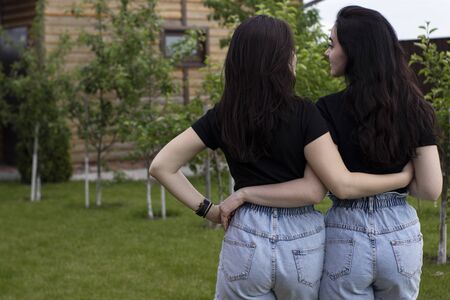 Two young brunette women in a black T-shirt and denim shorts hugging. Sisters, girlfriends. family...