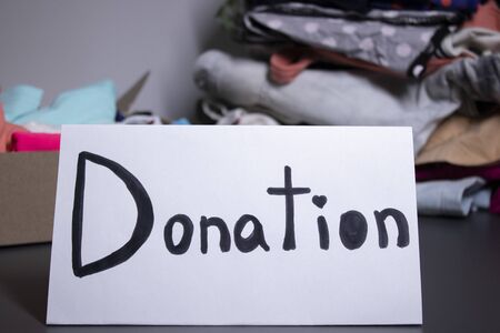 donation sign handwritten with black letters. A box with clothes and a pile of clothes nearby on a...