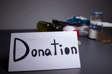 donation sign handwritten with black letters. A pile of food supplies on a grey table. Food donation...