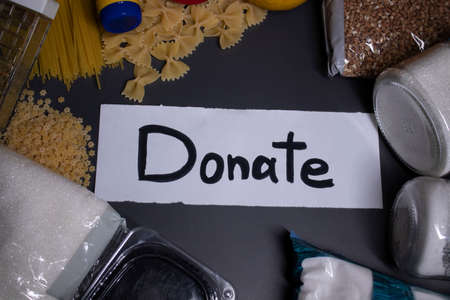 Donate sign handwritten with black letters. A pile of food supplies on a grey table. Food donation...