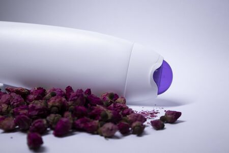 white shampoo bottle with purple neck and no label near a pile of little pink roses. body care and beauty concept. Copy space. High quality photoの写真素材