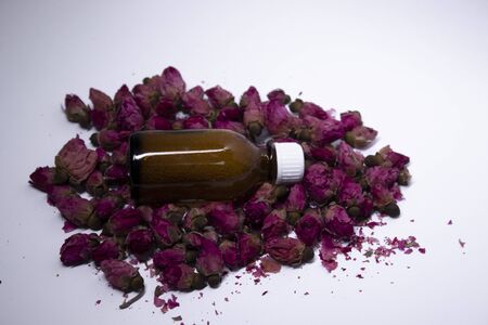 little liquid bottle with no label near a pile of little pink roses. body care and beauty concept. Copy space. High quality photoの写真素材
