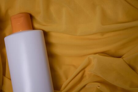 a yellow shampoo bottle with yellow neck and no label in a silk yellow fabric. body care and beauty...