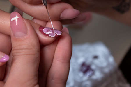 the process of doing manicure. Closeup of hands of professional manicurist, painting little flowers on nails. Concept of doing manicure. beauty concept. Gel polish, shellacの写真素材