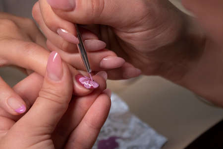 the process of doing manicure. Closeup of hands of professional manicurist, painting little flowers on nails. Concept of doing manicure. beauty concept. Gel polish, shellacの写真素材