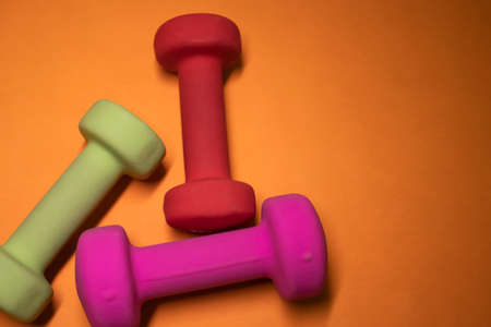 Bright pink, green and red small dumbbells on an orange background. Sport concept. High quality...