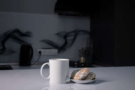 white cup with tea and sticking out tea bag next to gingerbread on white table in gray kitchen. High...