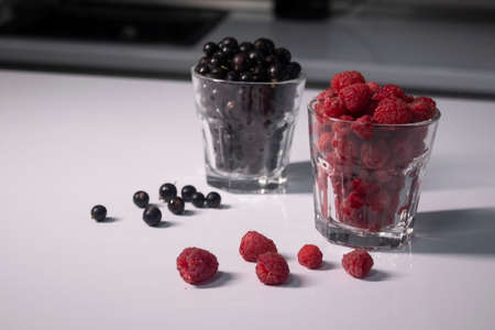 transparent glasses with currants and raspberries on a white table in a gray kitchen. High quality photoの写真素材