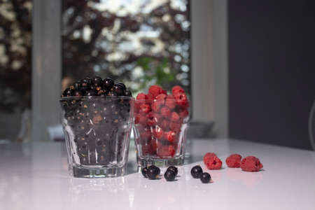 transparent glasses with currants and raspberries on a white table in a gray kitchen. High quality...