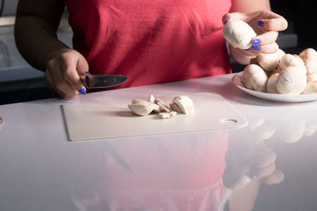 girls hands cut champignon mushrooms on a white plastic board on a white table top. cooking process....