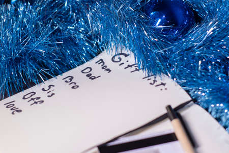 a notebook with title Gift list with a pen near a blue shiny tinsel for christmas tree. new years...