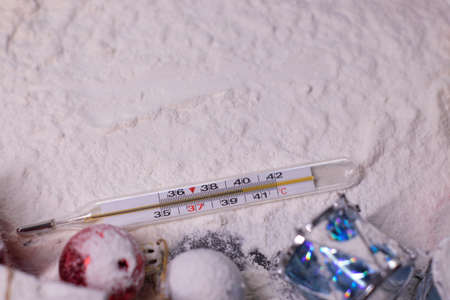 medical thermometer next to New Years decorations in the snow. Christmas trees, balls, snowflakes,...
