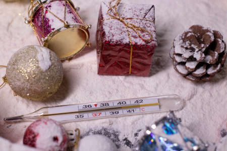 medical thermometer next to New Years decorations in the snow. Christmas trees, balls, snowflakes,...