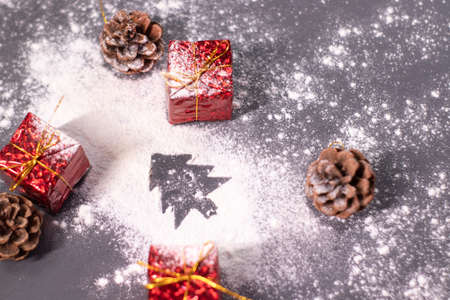 Christmas decorations, gifts and pine cones in the snow and the silhouette of a Christmas tree. Christmas mood. Flatly photo.の写真素材