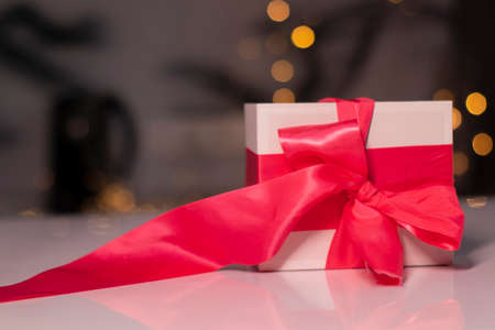 white gift box with pink ribbon bow on gold bokeh background.