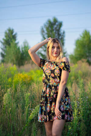 overlight bright portrait of a charming attractive blonde in flowery dress in the field.の写真素材