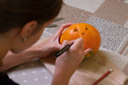 the process of making a Halloween pumpkin. cutting out the mouth by brunette girl.の写真素材