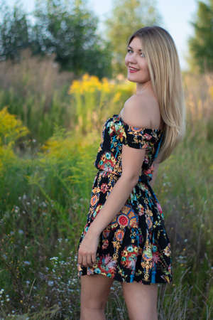 overlight bright portrait of a charming attractive blonde in flowery dress in the field.の写真素材