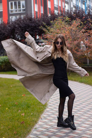 attractive slim young brunette in fashionable trench, black dress and sunglasses in park. autumn, yellow leaves.の写真素材