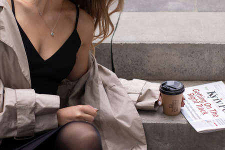 close up of a woman in trench coat near a paper cup coffee and a newspaper. urban lifestyle concept.