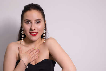 emotional portrait of attractive brunette in black top with white pearl earrings on white...