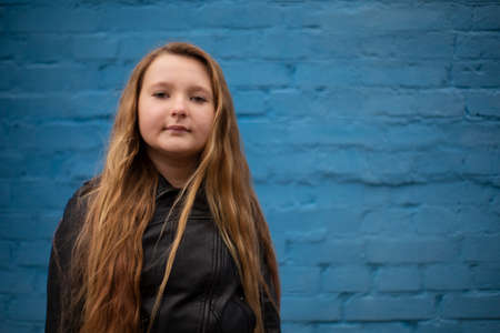 portrait of cute brunette teen girl in Leather Jacket on the background of blue brick wall ....