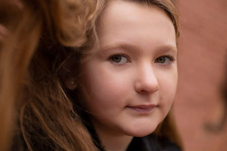 portrait of cute brunette teen girl in black fur coat on the background of brown brick wall ....