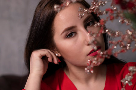 portrait of attractive brunette woman in red blouse near decorative sparkling red branches boquet. copy space. st valentinesの写真素材