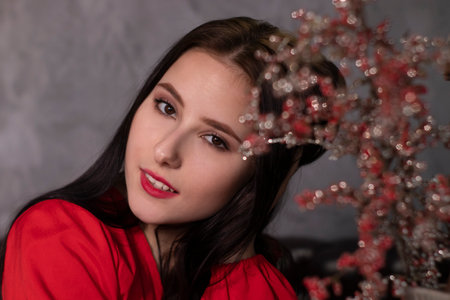 portrait of attractive brunette woman in red blouse near decorative sparkling red branches boquet....