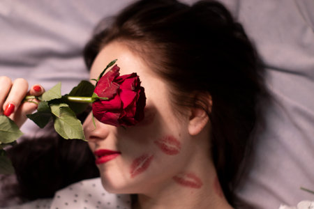 sexy brunette woman with kisses, lipstick marks on her face and neck, with red rose. girlfriend, date, relashionship. lesbian gay. lgbt. copy spaceの写真素材